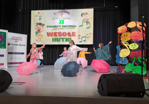 Grupa dzieci w kolorowych strojach podczas występu na scenie.