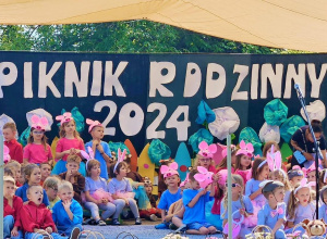 Dzieci w kolorowych strojach na tle napisu "Piknik Rodzinny".