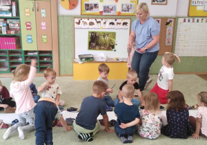 Dzieci siedzą na dywanie, słuchają pani pedagog, która przedstawia na czym będzie polegała zabawa.