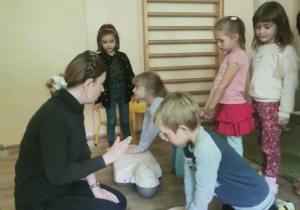 Prowadząca zajęcia obserwuje dwoje dzieci ćwiczące usiskanie klatki piersiowej przy resuscytacji (na fantomach).