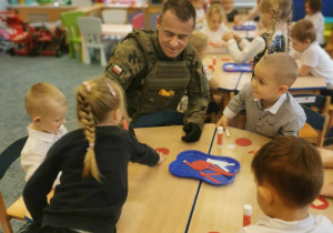 Dzieci z grupy IV razem z żołnierzem przy stoliku wykonują kotyliony.