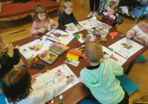 Dzieci przy stolikach projektują stroje dla postaci z "Królewny Śnieżki" z różnych materiałów plastycznych.