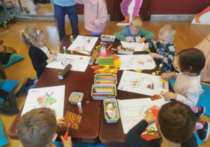 Dzieci przy stolikach projektują stroje dla postaci z "Królewny Śnieżki" z różnych materiałów plastycznych.