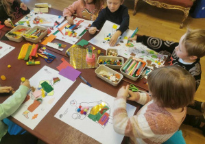 Dzieci przy stolikach projektują stroje dla postaci z "Królewny Śnieżki" z różnych materiałów plastycznych.