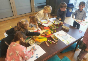 Dzieci przy stolikach projektują stroje dla postaci z "Królewny Śnieżki" z różnych materiałów plastycznych.