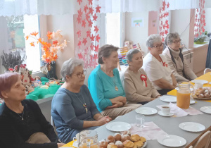 Seniorzy przy zastawionym stole podziwiają występy przedszkolaków.