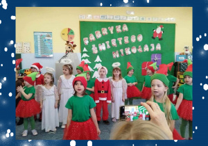 Grupa dzieci w świątecznych przebraniach podczas występu bożonarodzeniowego.