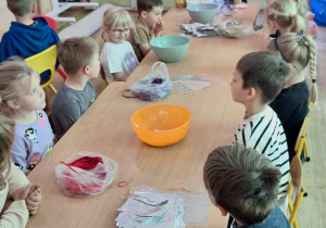 Dzieci słuchają prelekcji podczas warsztatów, na stolikach znajdują się składniki do wykonania kul.