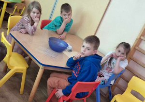 Dzieci słuchają prelekcji podczas warsztatów, na stolikach znajdują się składniki do wykonania kul.