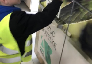 Chłopiec wrzuca plastikową butelkę do automatu zgniatającego.