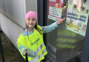 Dziewczynka wskazuję palcem plakat promujący zbieranie plastikowych butelek.