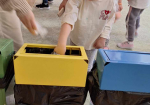 Dziewczynka wrzuca śmieci do odpowiedniego pojemnika do recyklingu.