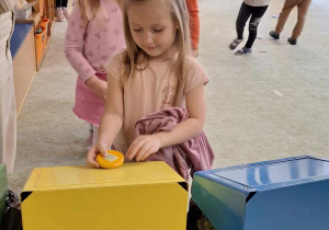 Dziewczynka wrzuca śmieci do odpowiedniego pojemnika do recyklingu.