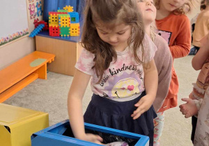 Dziewczynka wrzuca śmieci do odpowiedniego pojemnika do recyklingu.
