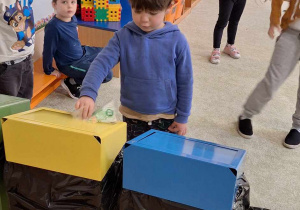 Chłopiec wrzuca śmieci do odpowiedniego pojemnika do recyklingu.