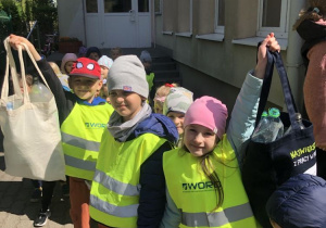 Dzieci trzymające ekologiczne torby wypełnione plastikowymi butelkami.