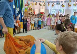 Duża grupa dzieci stoi w kole i wybiera kolorowe balony, rozdawane przez organizatora spotkania.