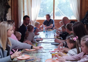 Dzieci wraz z rodzicami siedzą przy stołach i formują wspólnie ciasto na chleb.