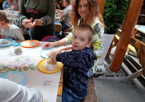 Mama z dzieckiem siedzą przy stole i formują ciasto na chleb.