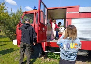Dzieci znajdują się w wozie strażackim, wokół wozu stoją rodzice dzieci.