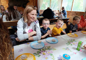Dzieci wraz z rodzicami siedzą przy stołach i formują wspólnie ciasto na chleb.