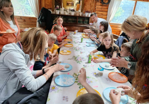 Dzieci wraz z rodzicami siedzą przy stołach i formują wspólnie ciasto na chleb.