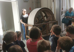 Pani oprowadzająca grupę dzieci po teatrze demonstruje urządzenie do robienia odgłosu wiatru