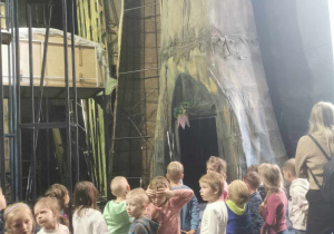 Grupa dzieci podziwia elementy teatralnej dekoracji - drzewo.