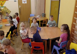 Grupka dzieci siedzi przy stole i słucha informacji dotyczących zdrowia i higieny