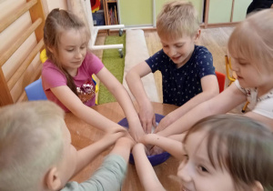Grupka dzieci siedzi przy stole i mieszają rękoma składniki na kule do kąpieli