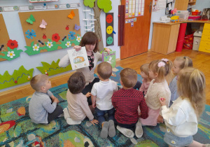 Na dywanie siedzi pani z grupą dzieci i pokazuje im książeczki, które będzie im czytała.